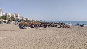 Une plage avec des transats et des parasols, des palmiers et des bâtiments en arrière-plan.