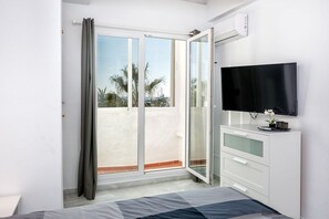Un dormitorio con cama, televisión, puerta corrediza de vidrio a un balcón y cómoda blanca.