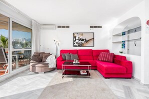 A modern living room with a red sofa, a coffee table, and a large window offering a city view.
