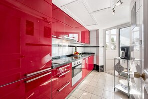 Una cocina moderna con armarios rojos, estufa de acero inoxidable y una cafetera.