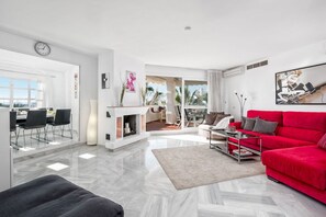 Una sala de estar moderna con un sofá rojo, un comedor con sillas, una chimenea y vistas a través de la puerta de cristal.