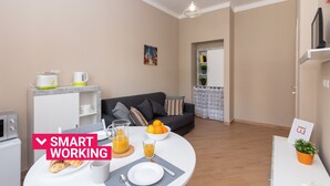 Un salon moderne avec un coin repas, comprenant un canapé, une table basse et un espace dédié au petit-déjeuner avec du jus d’orange et des viennoiseries.