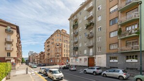 Un immeuble résidentiel à plusieurs étages doté de balcons, une rue bordée de voitures garées et un ciel dégagé.
