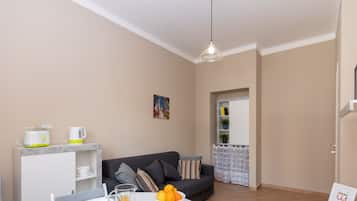 A modern living room with a dining area, featuring a sofa, coffee table, and a breakfast setup with orange juice and pastries.