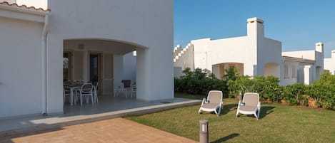 A modern villa with a patio, outdoor seating, and a well-maintained lawn.