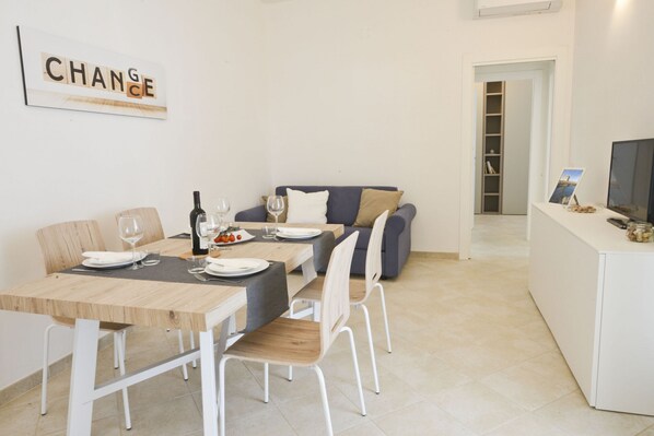 A modern dining area with a wooden table, white chairs, and a grey sofa. A framed sign with the word "CHANGE" is on the wall. - Blue Sea Villas Seafront by Wonderful Italy (Ostuni)