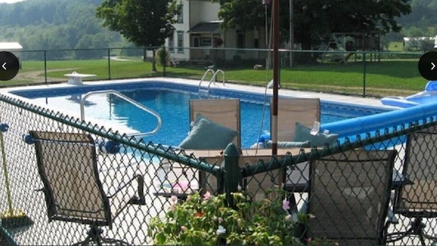 En swimmingpool med et hegn, liggestole og en parasol.