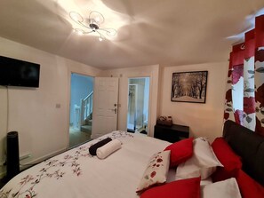A bedroom with a bed, a television, a door, and a painting.