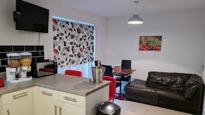 En kompakt opholdsstue med tekøkken, spiseplads og siddeområde med sofa.