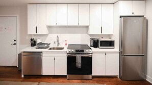 A modern kitchen with white cabinets, a stainless steel refrigerator, a microwave, a stove, and a dishwasher. - Unit 102 · Near Yale and Downtown Newly Renovated (New Haven)