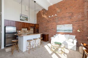 Enjoy a warm and inviting space with a kitchen and living area featuring a brick wall, stainless steel appliances, and a central island with bar stools.