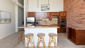 A modern kitchen with a central island, bar stools, stainless steel appliances, and a brick accent wall.