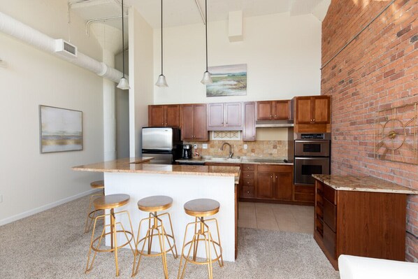 Una cocina moderna con una isla central, taburetes de bar, electrodomésticos de acero inoxidable y una pared decorativa de ladrillo.