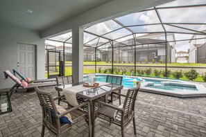 Ein überdachter Patio-Bereich mit Glasverkleidung, einem Pool und Gartenmöbeln.