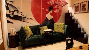 A living room with a green sofa, a small table, and a decorative wall with a cherry blossom design. - Wabi Sabi B&B - a Japanese Sleep Oasis in Belgium (Peer)