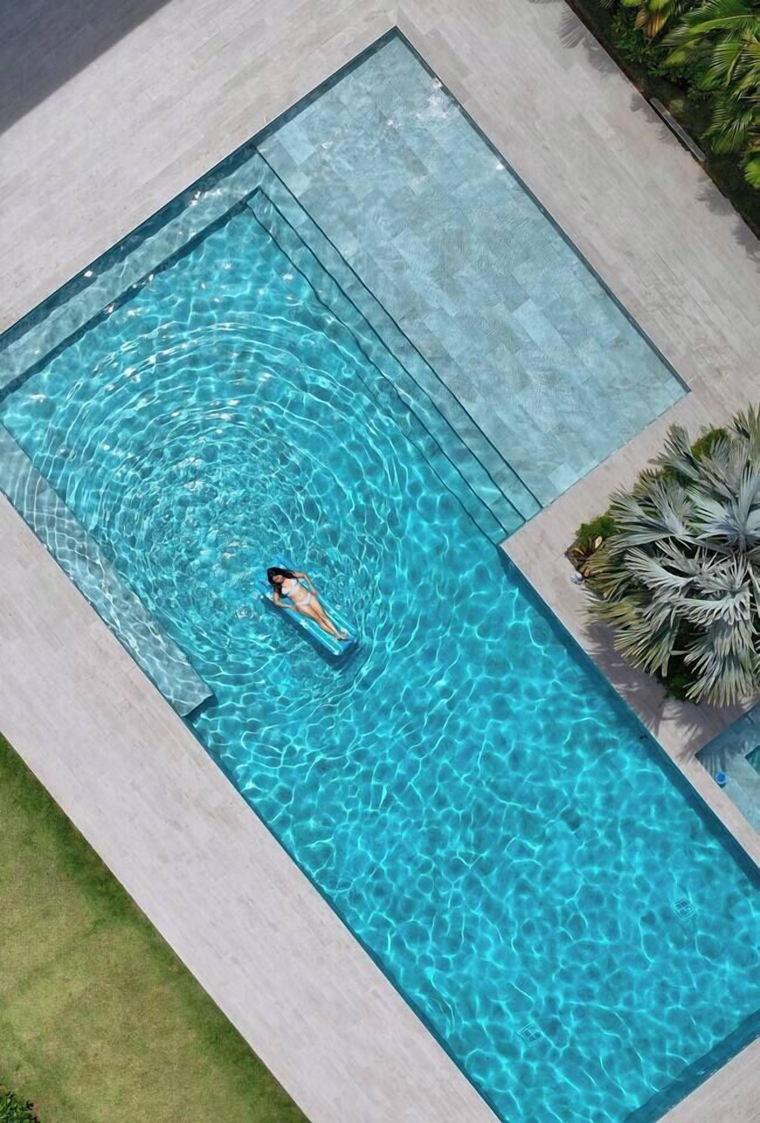 Ein rechteckiger Swimmingpool mit klarem, blauem Wasser, umgeben von einer hell gefliesten Terrasse.