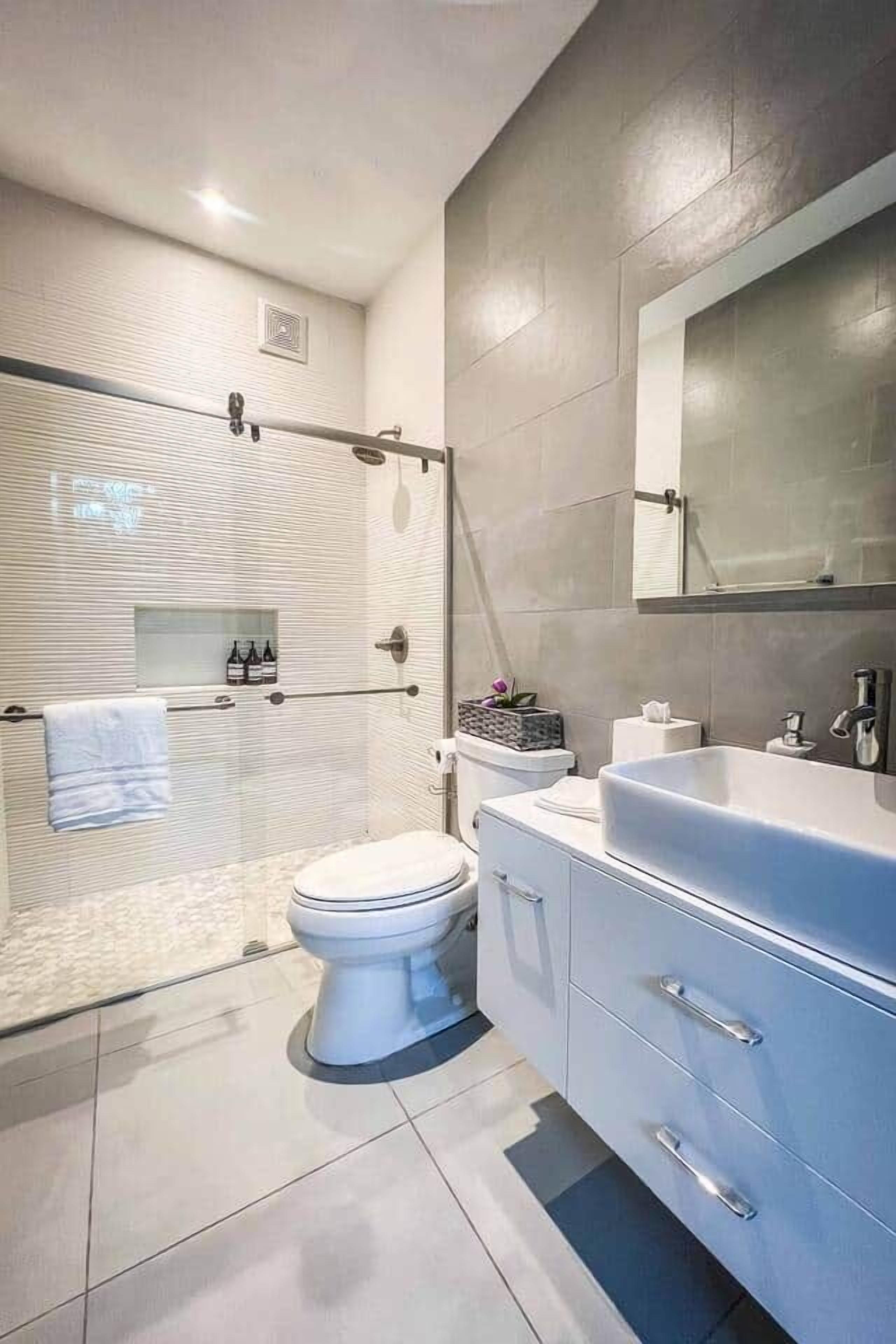 Een moderne badkamer met een douchecabine van glas, een wit toilet, een wastafel met spiegel en een betegelde vloer.