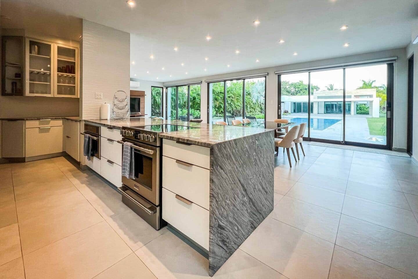 A modern kitchen with an island, built-in oven, and large windows offering a view of the outdoors.