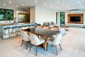 Een moderne keuken met een centraal eiland, barkrukken, een eettafel met stoelen, een zithoek en een aan de muur bevestigde televisie.
