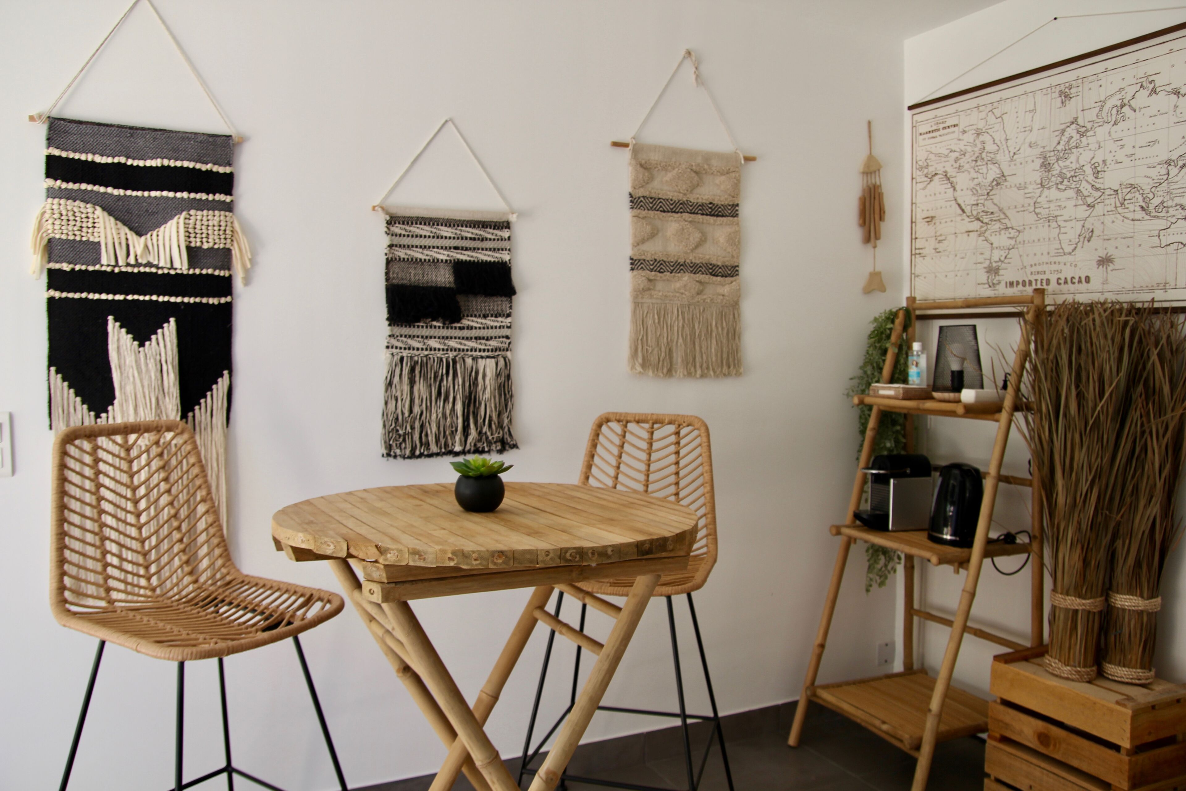 A room with a round wooden table, two wicker chairs, and three wall hangings.