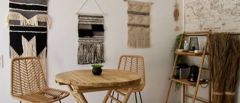 A room with a round wooden table, two wicker chairs, and three wall hangings.