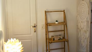 A bedroom with a bed, a bedside lamp, a wooden ladder shelf, a dreamcatcher, and a sign above the door.