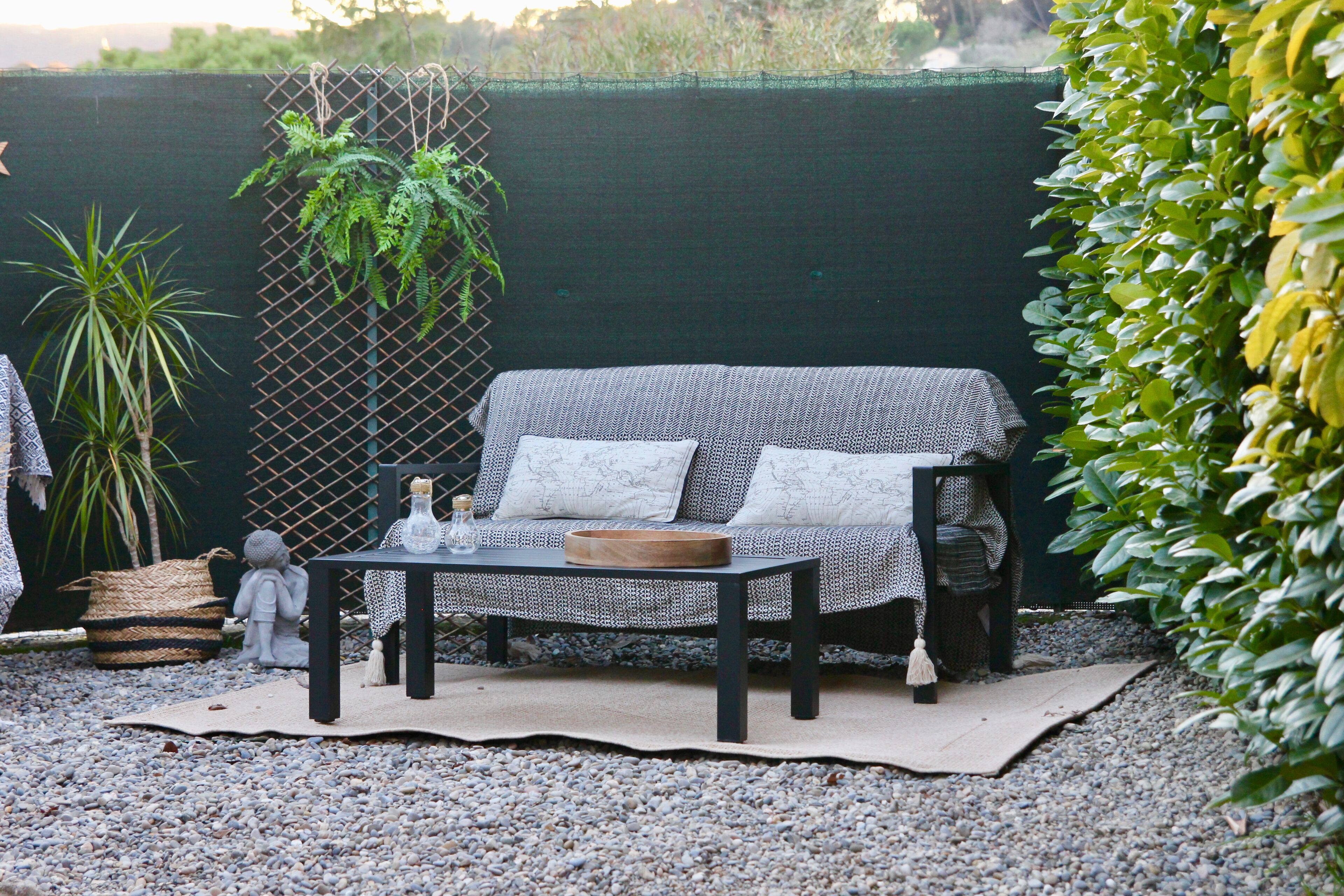 An outdoor seating area with a woven sofa, a table with a woven tablecloth, and decorative items.