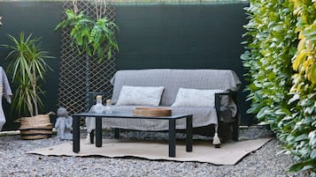 An outdoor seating area with a woven sofa, a table with a woven tablecloth, and decorative items.