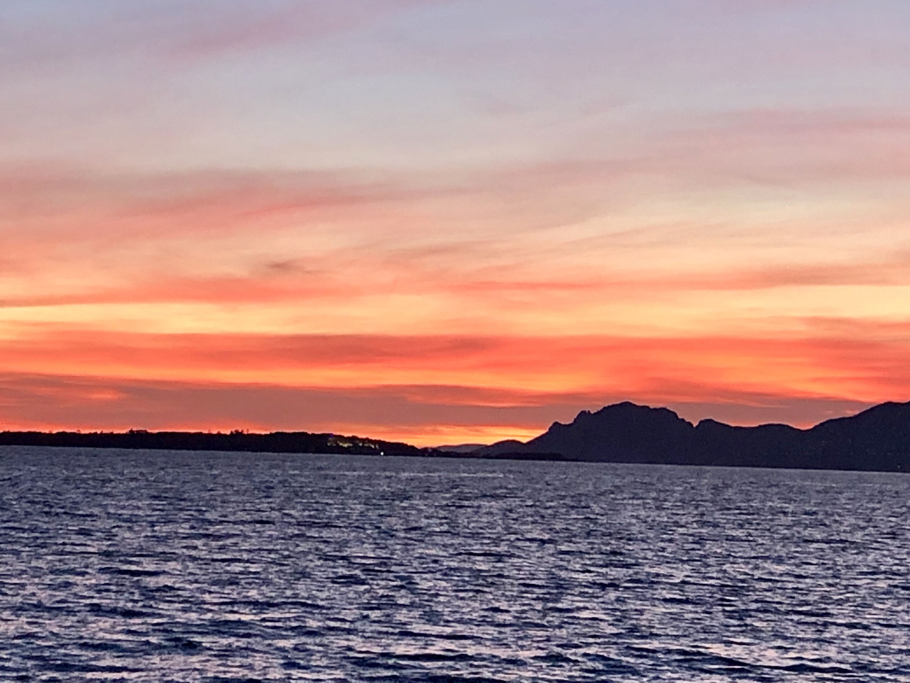 Tramonto su uno specchio d'acqua con montagne in lontananza.