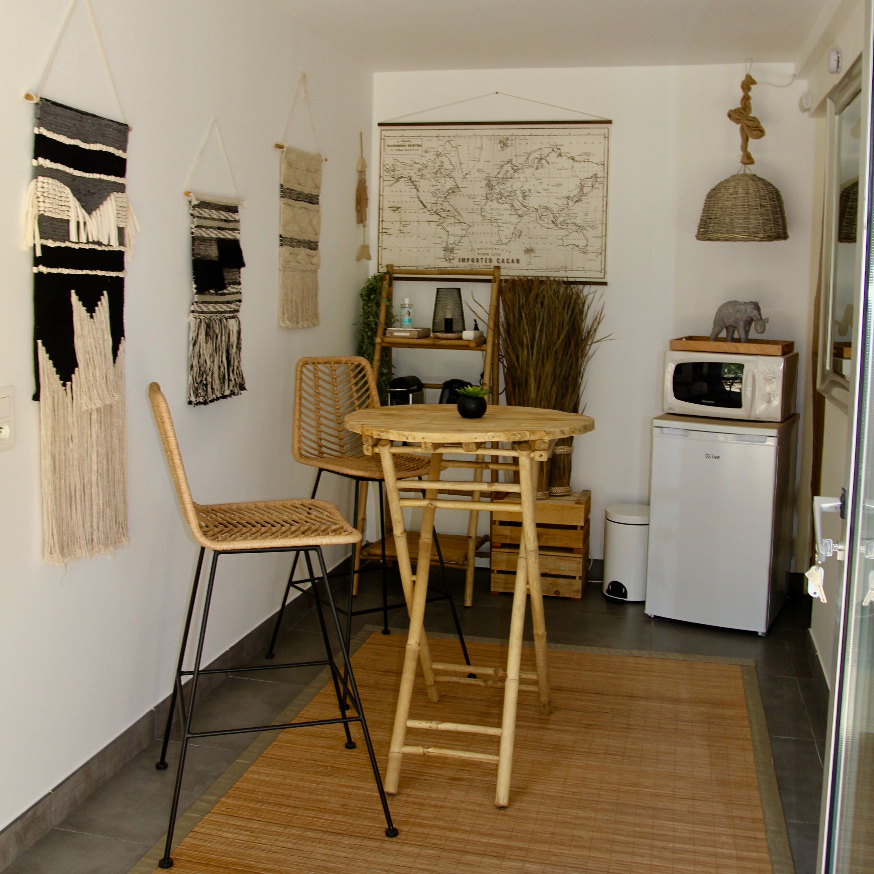 A compact kitchen with a wooden table and chairs, a small refrigerator, and decorative wall hangings.