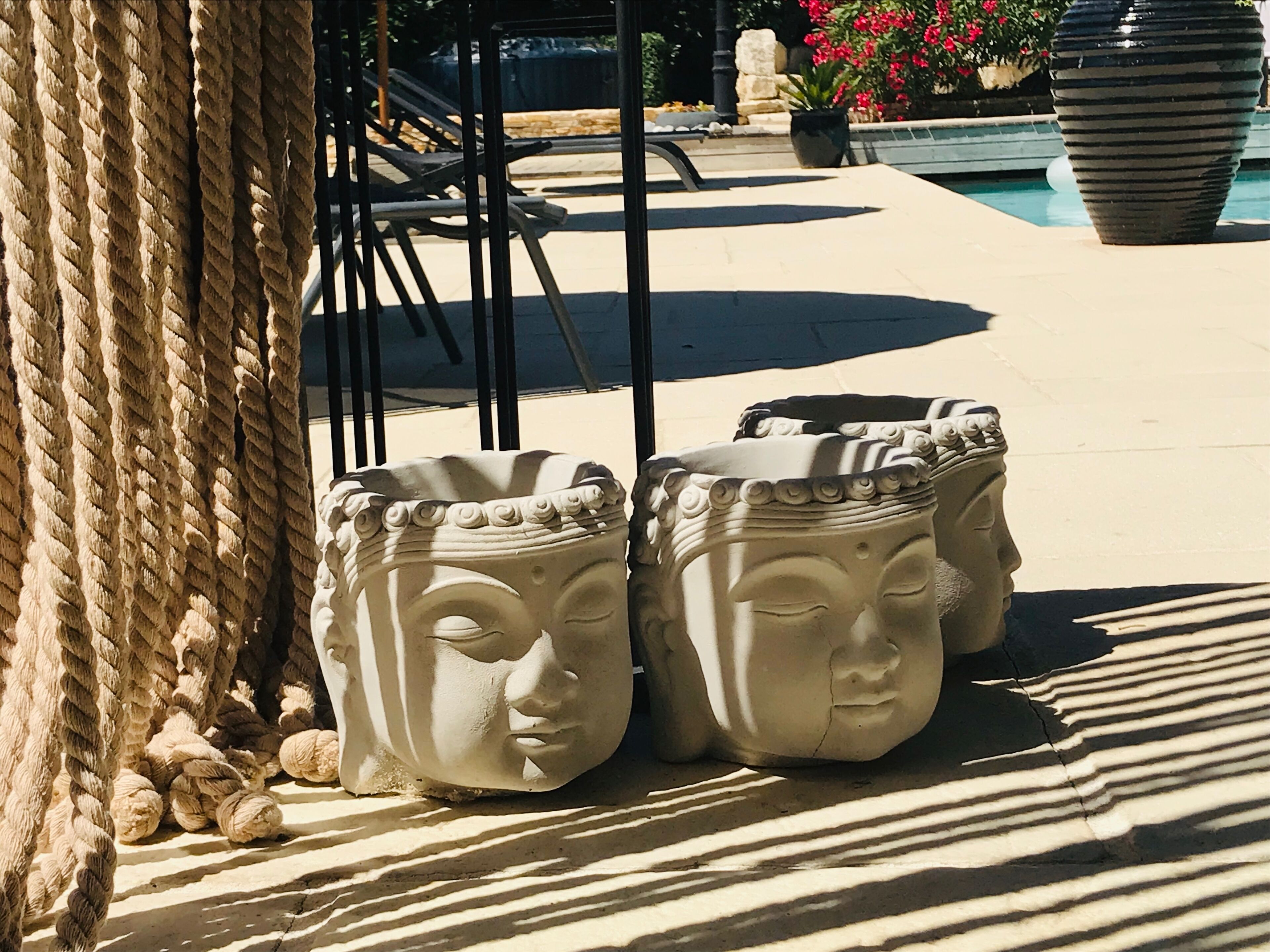 Outdoor stone planters with a classical design, a rope barrier, and a pool area in the background.