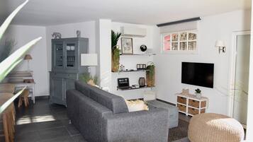 Un salon moderne avec un canapé gris, un pouf rond en fibres tressées, un téléviseur à écran plat et un meuble gris.