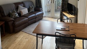 Una sala de estar acogedora con un sofá de cuero marrón, una mesa de comedor de madera y un televisor sobre un mueble de madera.