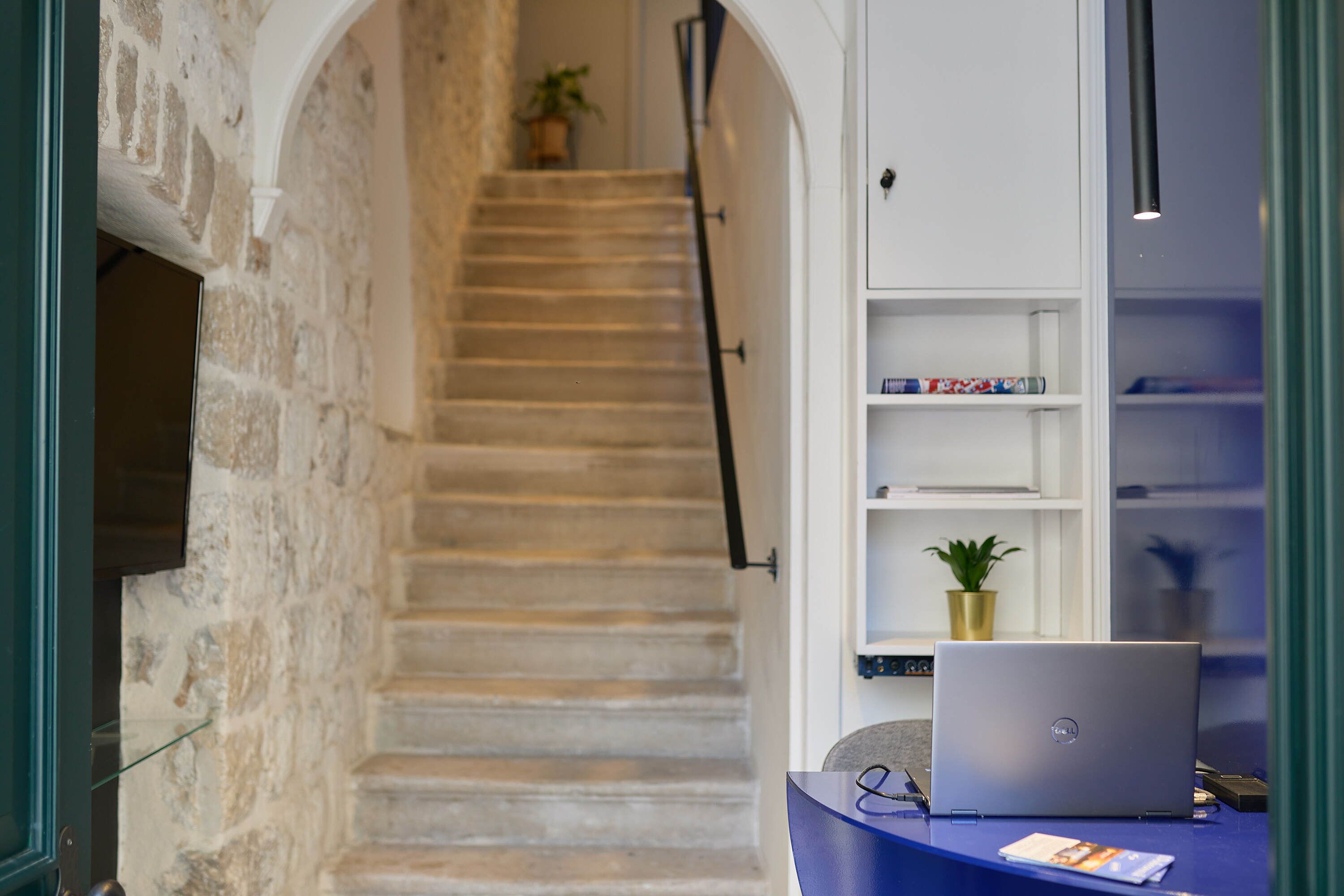 A staircase leading to a landing with a laptop on a desk, shelves with books, and a potted plant.
