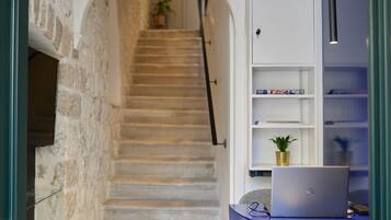 A staircase leading to a landing with a laptop on a desk, shelves with books, and a potted plant.