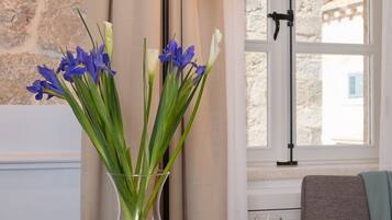 A breakfast table with a variety of food items, a vase with flowers, and a view of a stone wall and window.