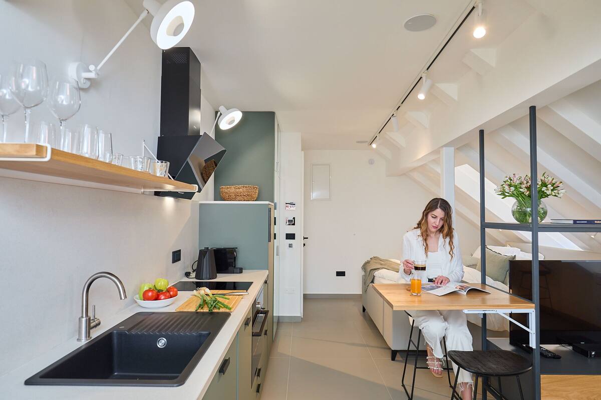 A modern kitchen with a built-in sink, a dining area with a table and chairs, and a living space with a sofa and a TV.