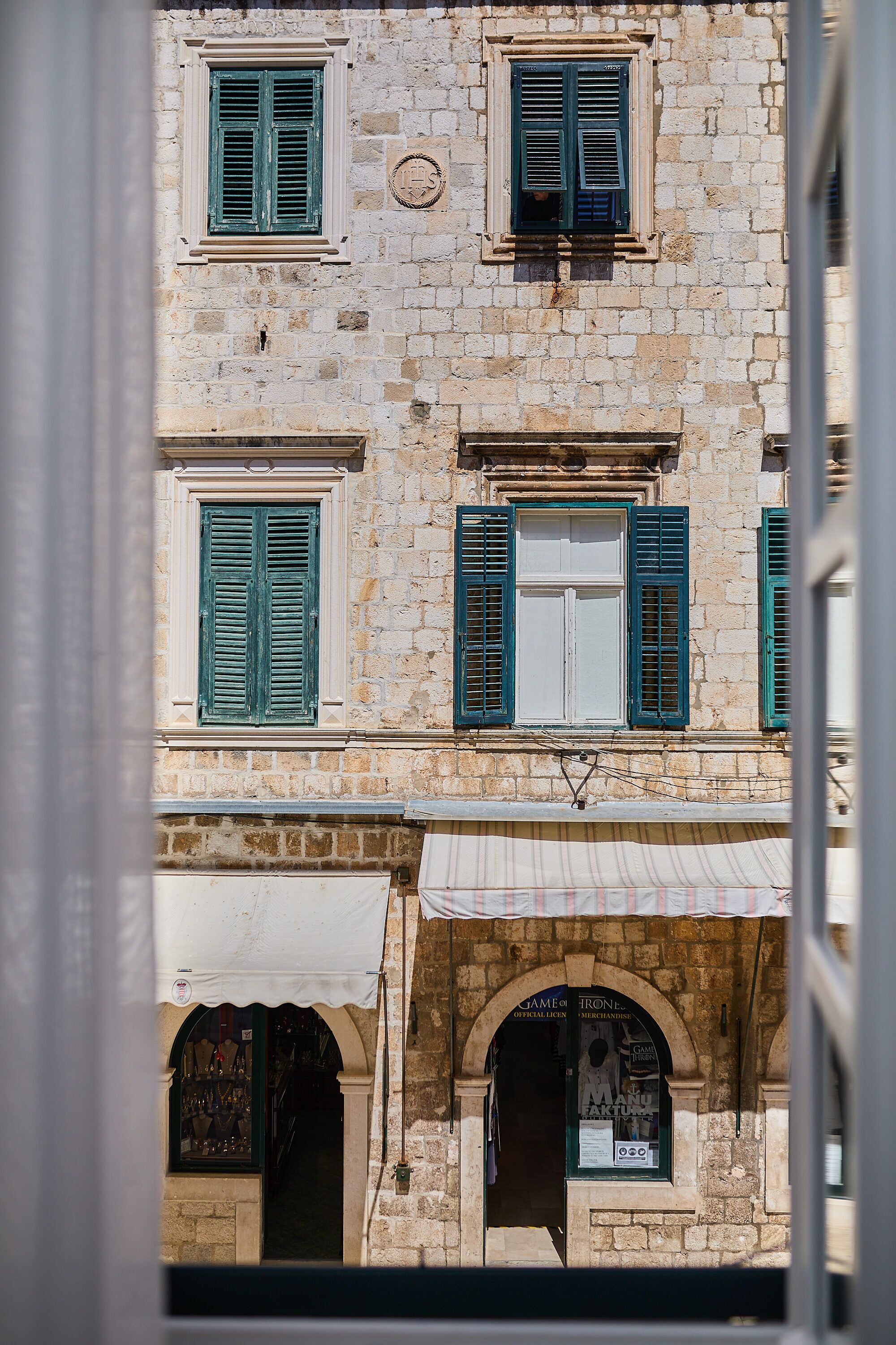 Un edificio con varias ventanas, algunas con contraventanas, y un escaparate con toldo.