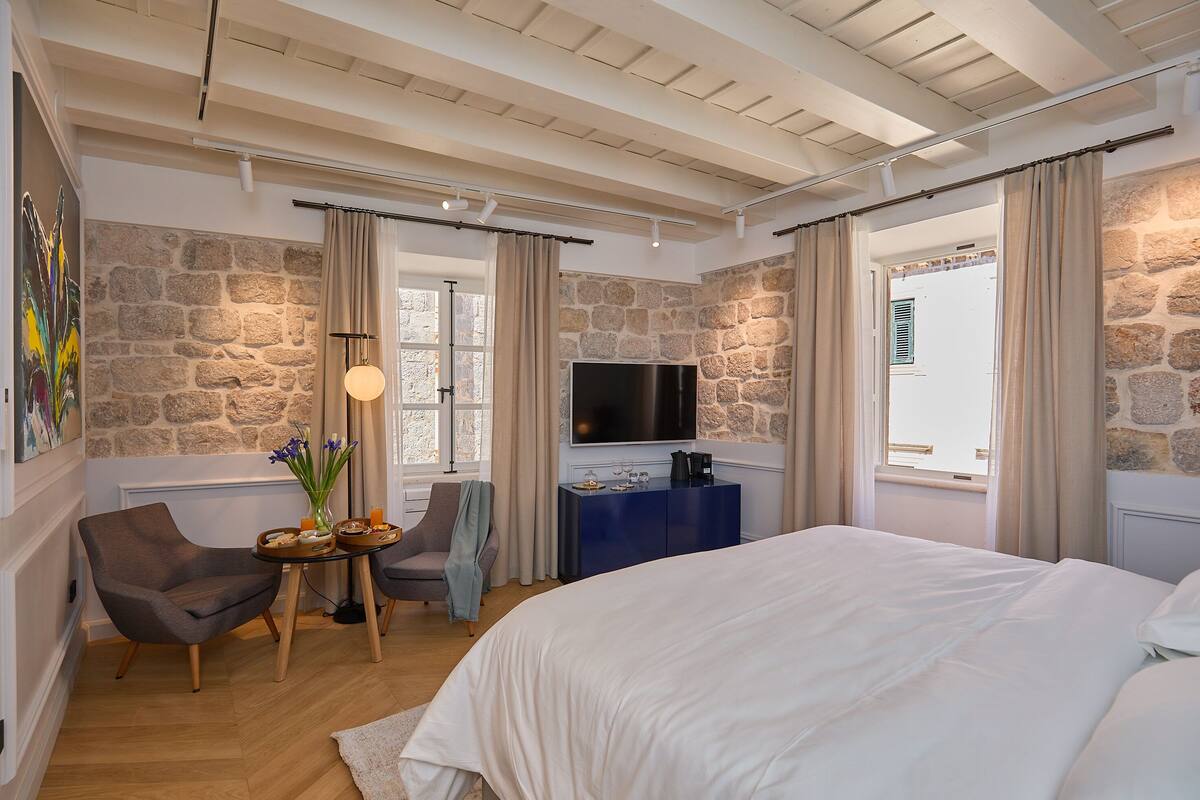 A bedroom with a stone wall, a bed, a TV, and a desk with a lamp.
