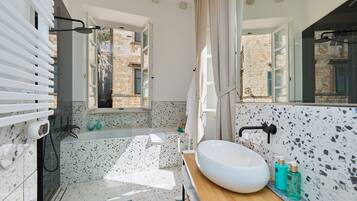 Ein modernes Badezimmer mit freistehender Badewanne, einem großen Spiegel und Blick auf einen Innenhof durch ein offenes Fenster.