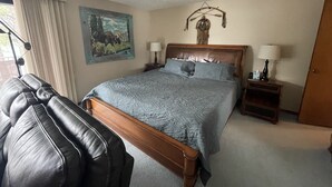 A hotel room with a large bed, a wooden headboard, two bedside lamps, a painting of a moose, a luggage rack, and a door. - Beautiful Lake Front Property  (Bayview)