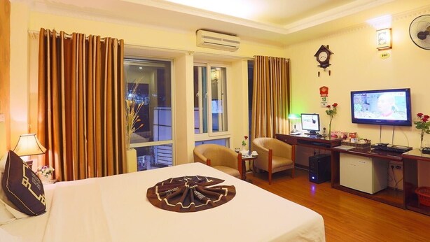 A hotel room with a bed, a desk with a computer, a television, and a view of the city at night. - Hanoi Palace Hotel (Hanoi)