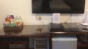 A hotel room with a large flat-screen TV mounted on the wall, a small refrigerator, a desk with a basket of snacks, and a framed picture above the TV. - Hanoi Palace Hotel (Hanoi)