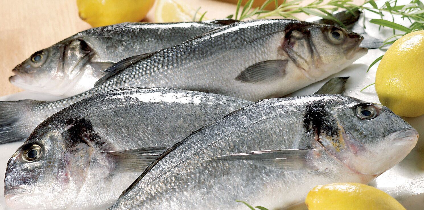 Three fish on a plate with lemon wedges and herbs.