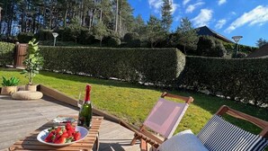 Een houten terras met een tafel gedekt voor twee personen, een fles champagne en een bord aardbeien.
