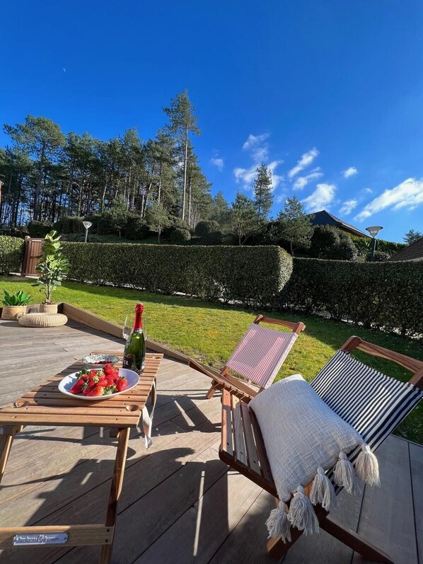 Una terraza de madera con una mesa lista para dos personas, una botella de champán y un plato de fresas.