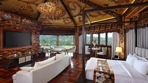 Una camera d'albergo lussuosa con un grande letto, un divano, una TV e un balcone con vista sul verde.