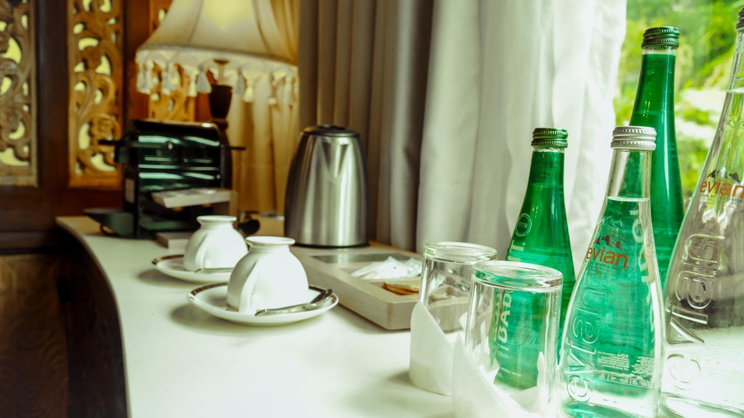 Ett hotellrum med en kaffebryggare, ett teservis och flaskor med grönt vatten på bordet.