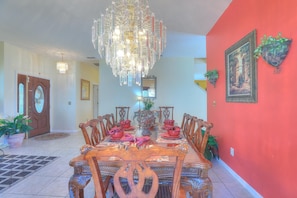 A dining area with a wooden table set for four, surrounded by chairs, a chandelier, and potted plants.