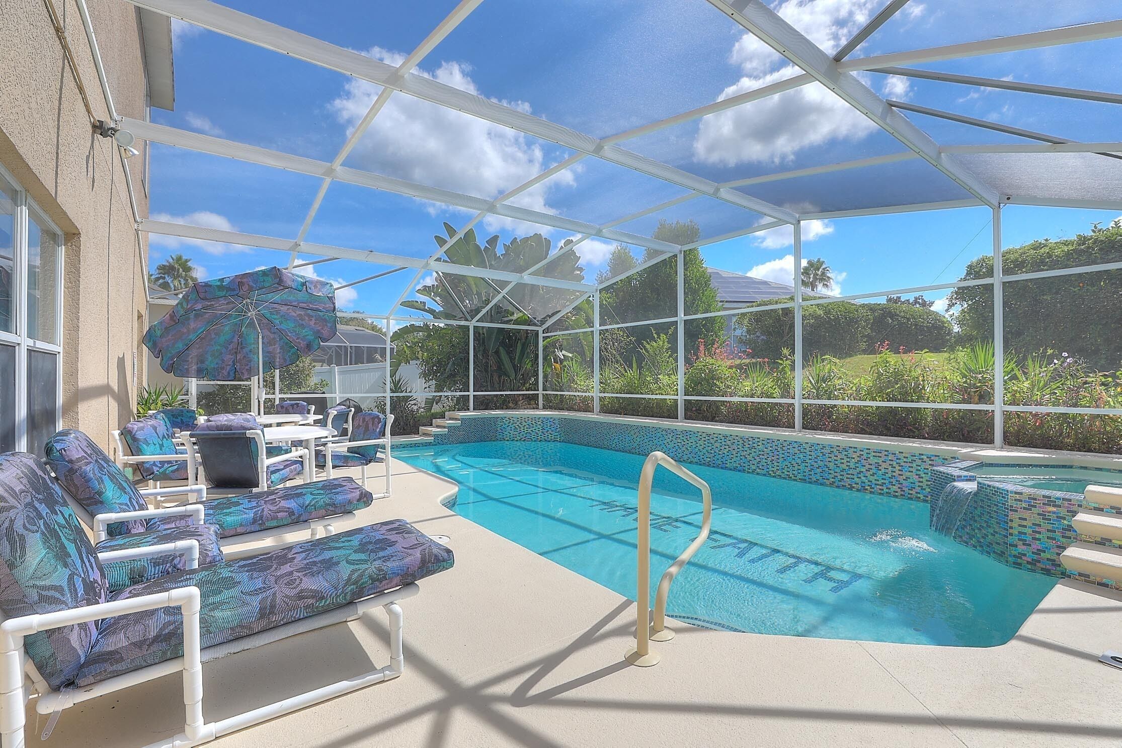 A covered outdoor swimming pool with lounge chairs and an umbrella.